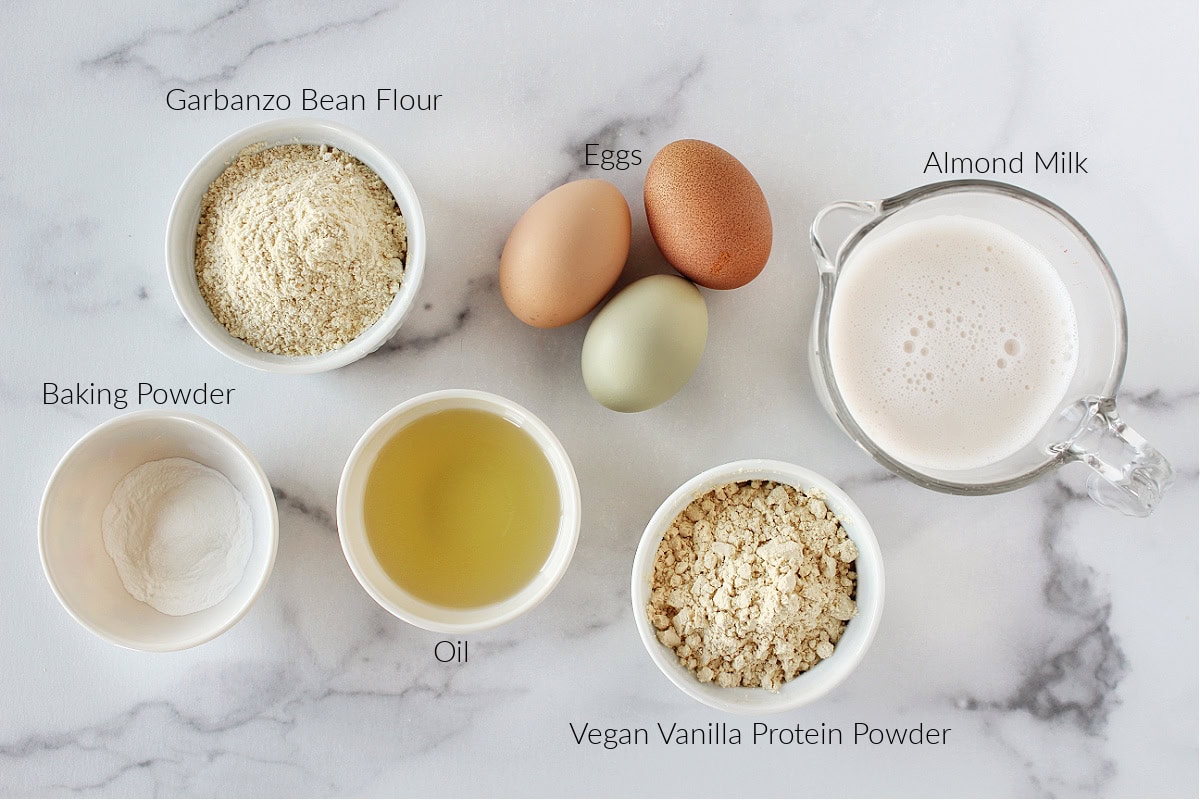 Labeled ingredients for protein powder pancakes on a white marble countertop.