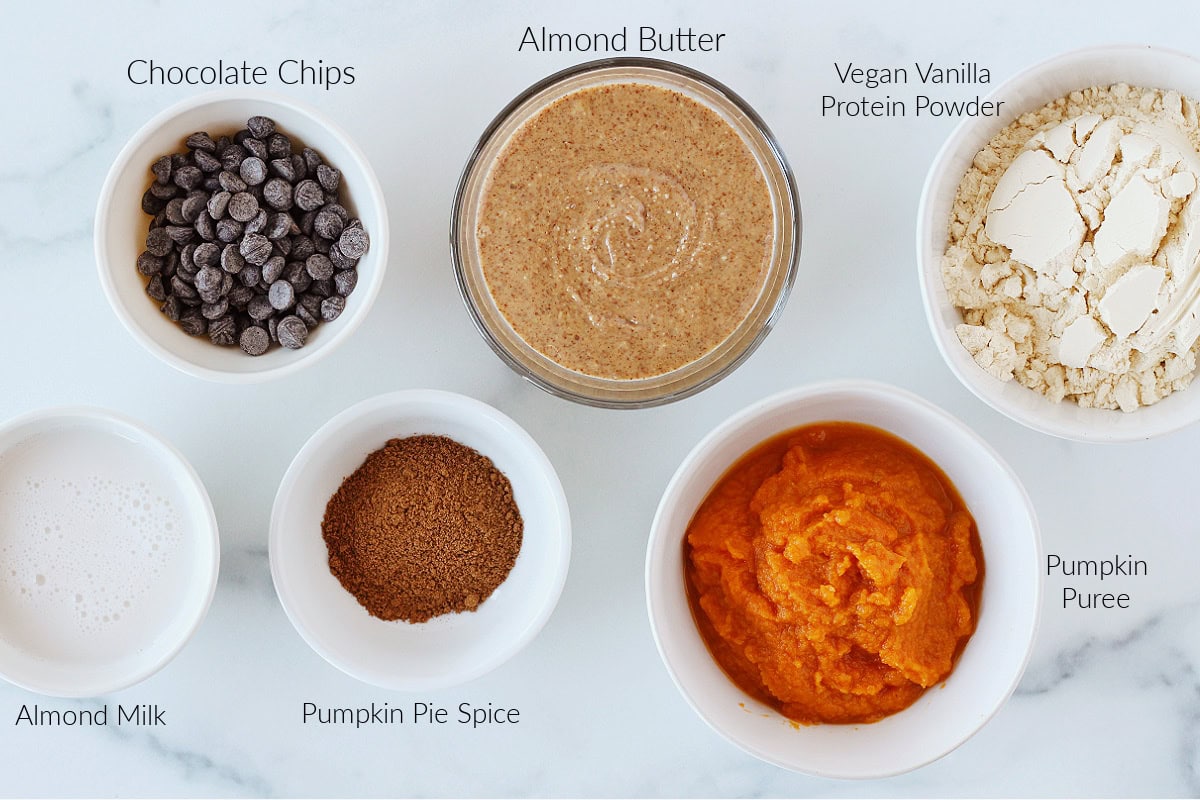 Labeled ingredients for pumpkin cookie dough on a white marble countertop.