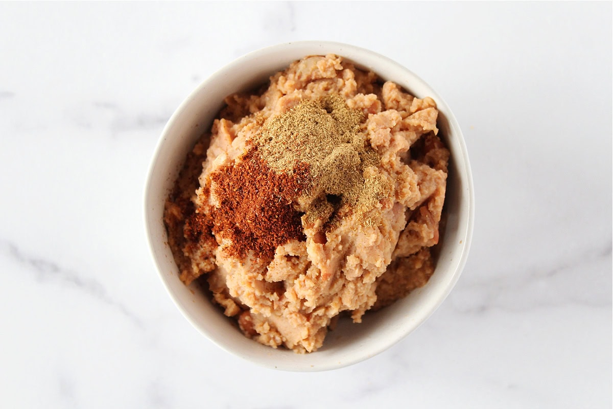 Cumin and chili powder sitting atop refried beans in a bowl.