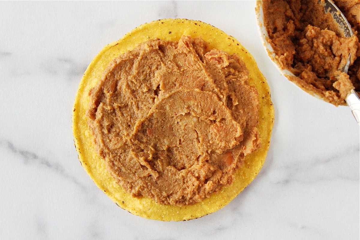 Refried beans spread thinly onto a corn tostada shell.