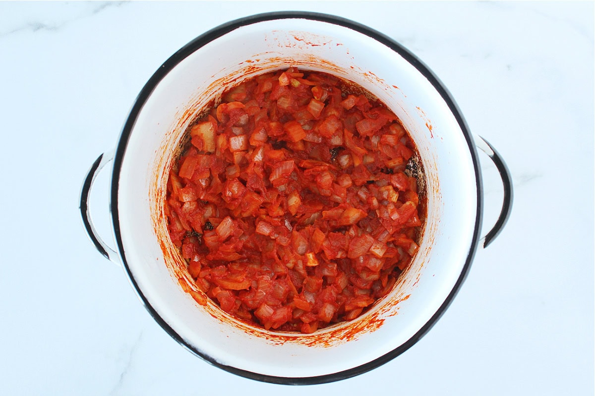 Sauteed onions, garlic and tomato paste in a white soup pot.