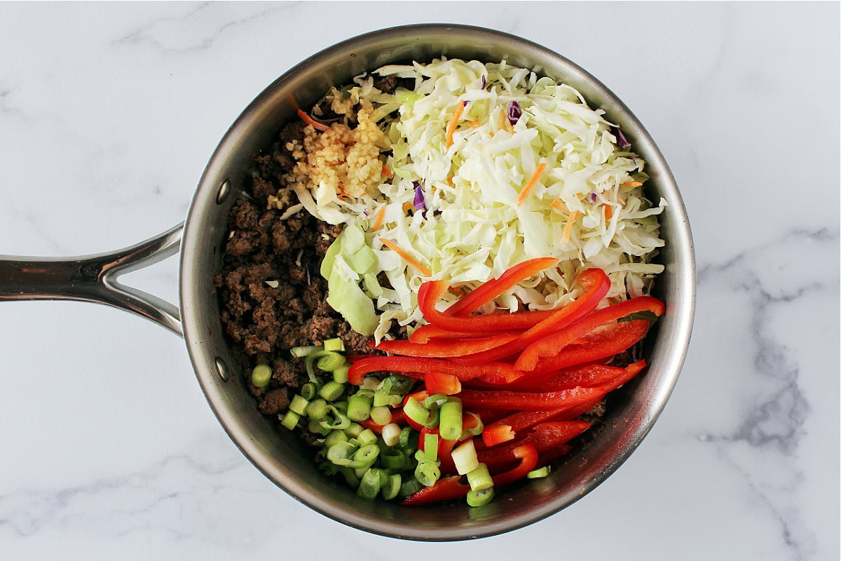 Browned ground sausage, green onion, coleslaw mix, and green onion in a sauté pan.