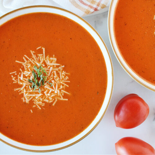 Two bowls of creamy tomato basil soup topped with shredded parmesan cheese.