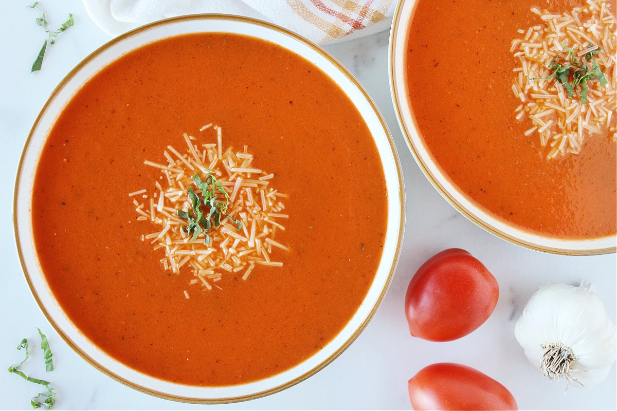 Two bowls of creamy tomato basil soup topped with shredded parmesan cheese.