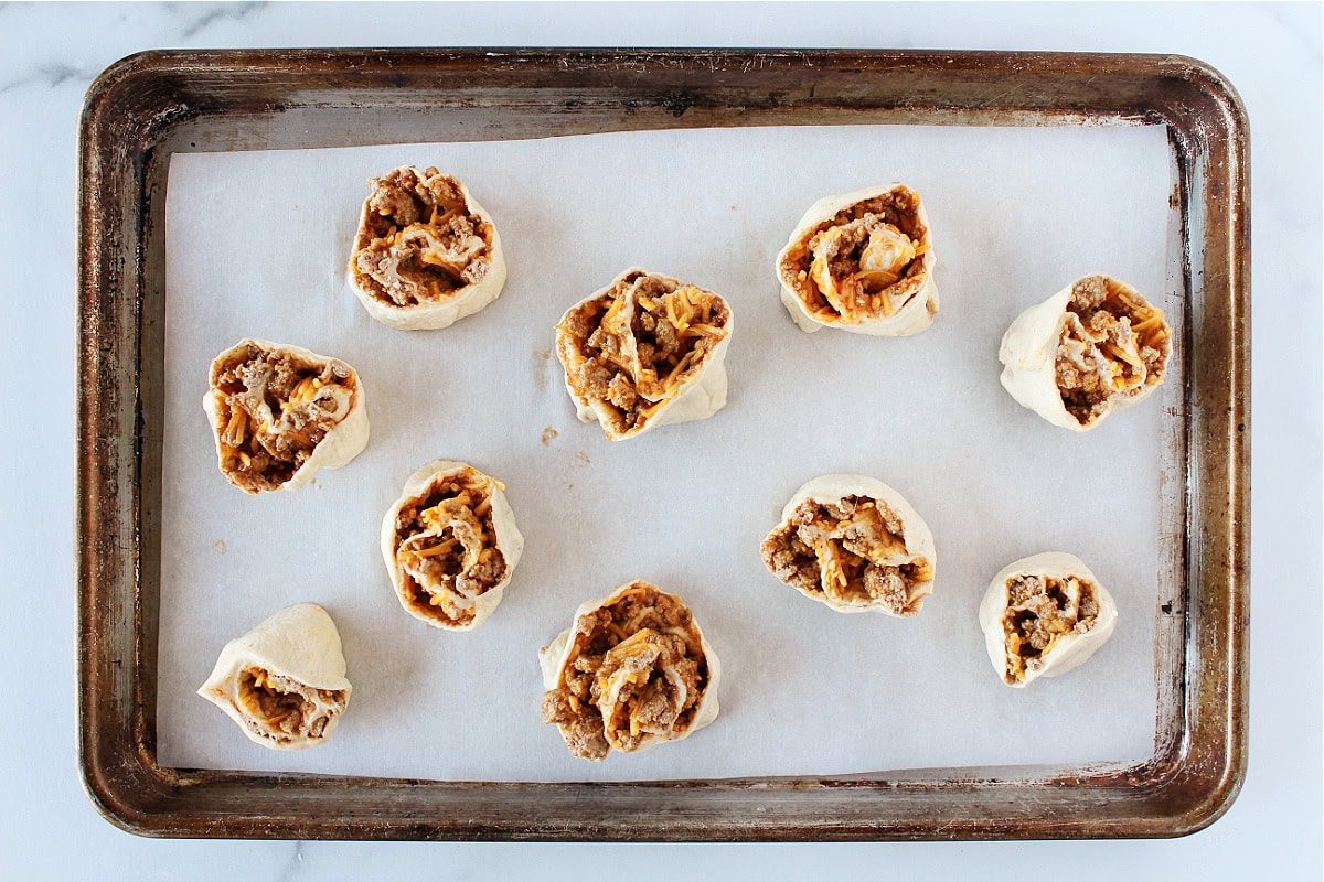 Unbaked sloppy joe crescent roll cups on a baking sheet.