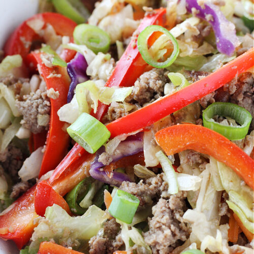 Sliced red bell peppers, green onions, and turkey sausage and coleslaw mix in a bowl.