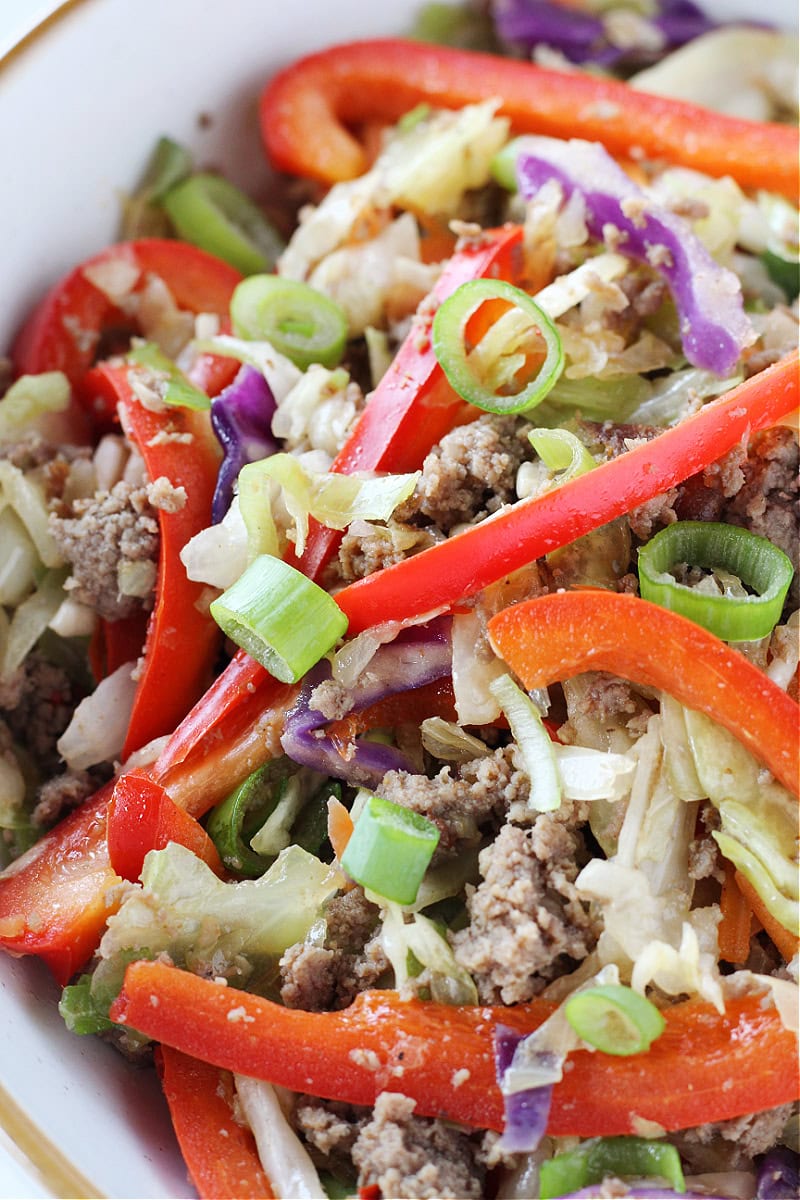 Sliced red bell peppers, green onions, and turkey sausage and coleslaw mix in a bowl.