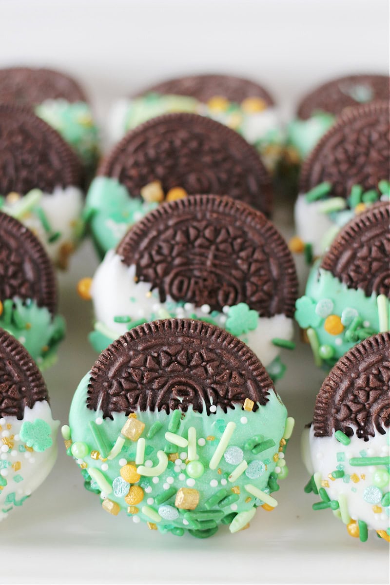 Half dipped Oreo cookies in green chocolate and white chocolate on a tray.