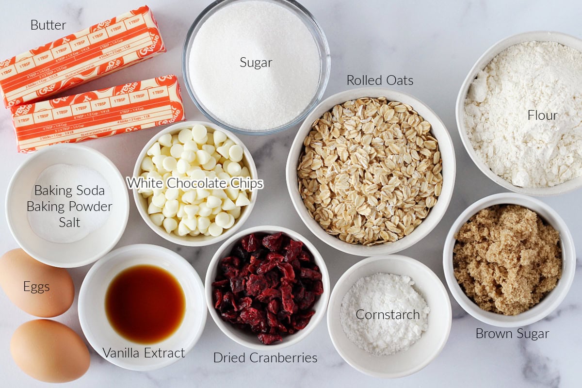 Labeled ingredients for oatmeal cranberry cookies on a white marble countertop.