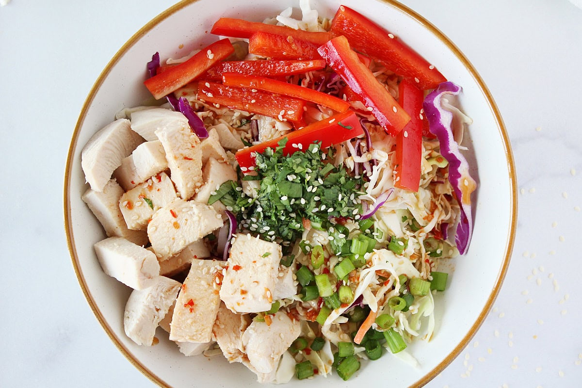 Asian dressing poured over fresh vegetables and sesame seeds in a bowl.