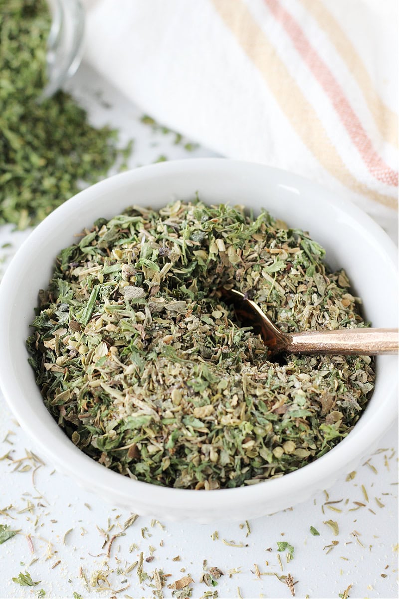 Homemade Italian seasoning in a white bowl with a small copper spoon.