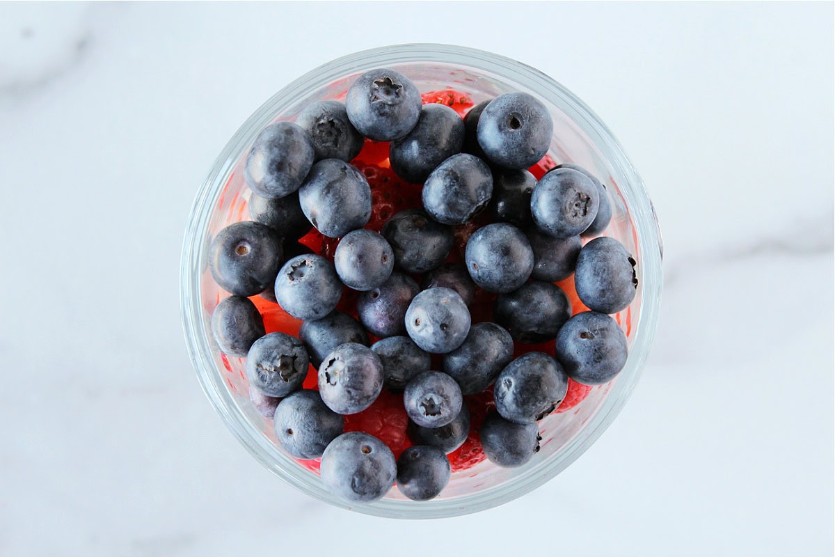 Blueberries on top of strawberries in a glass.