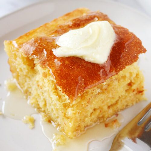 A piece of cornbread topped with butter and honey on a white plate.