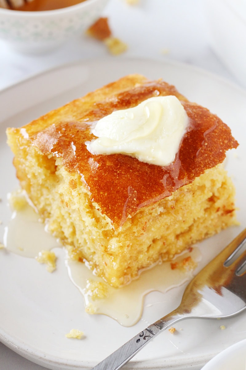 A piece of cornbread topped with butter and honey on a white plate.