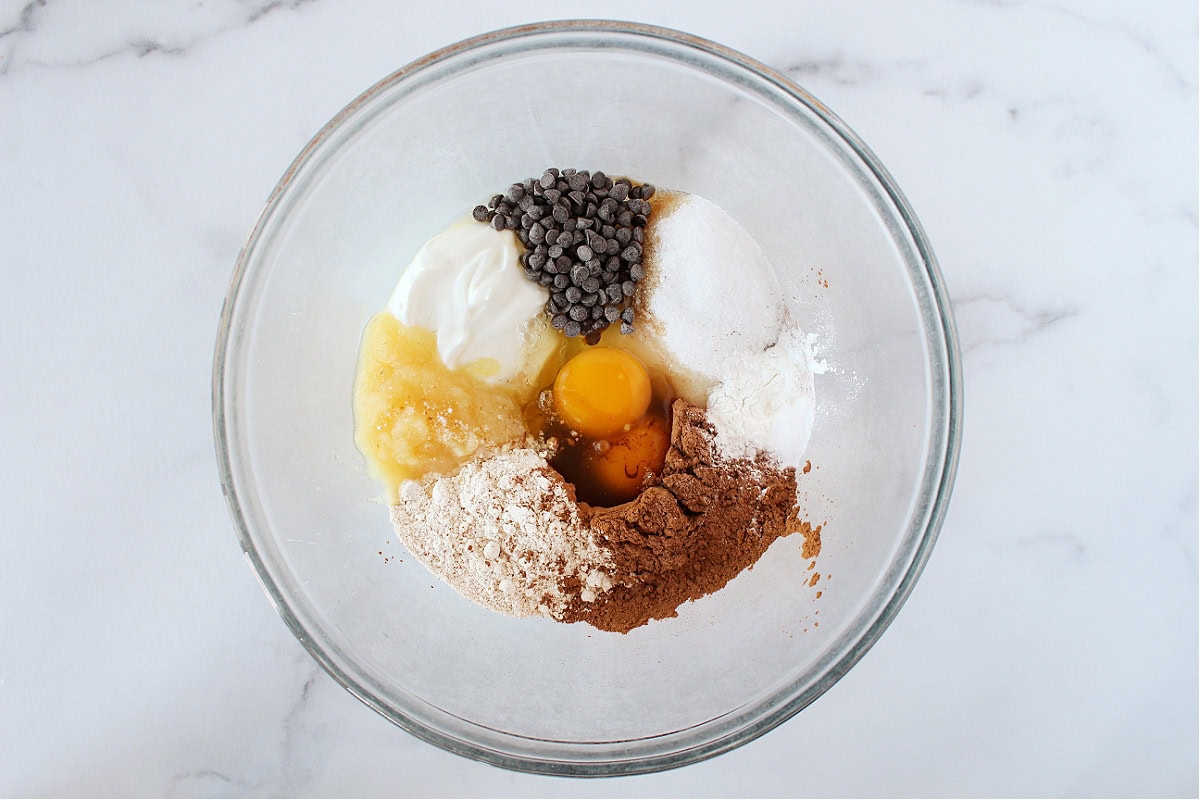 Eggs, Greek yogurt, oat flour, applesauce, cocoa powder and chocolate chips in a bowl.