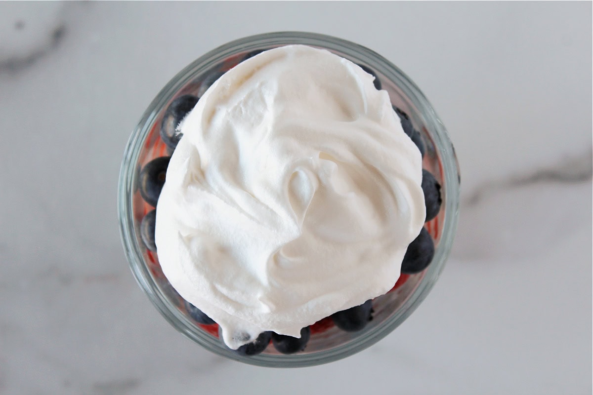 A dollop of whipped cream or Cool Whip on top of blueberries in a glass.