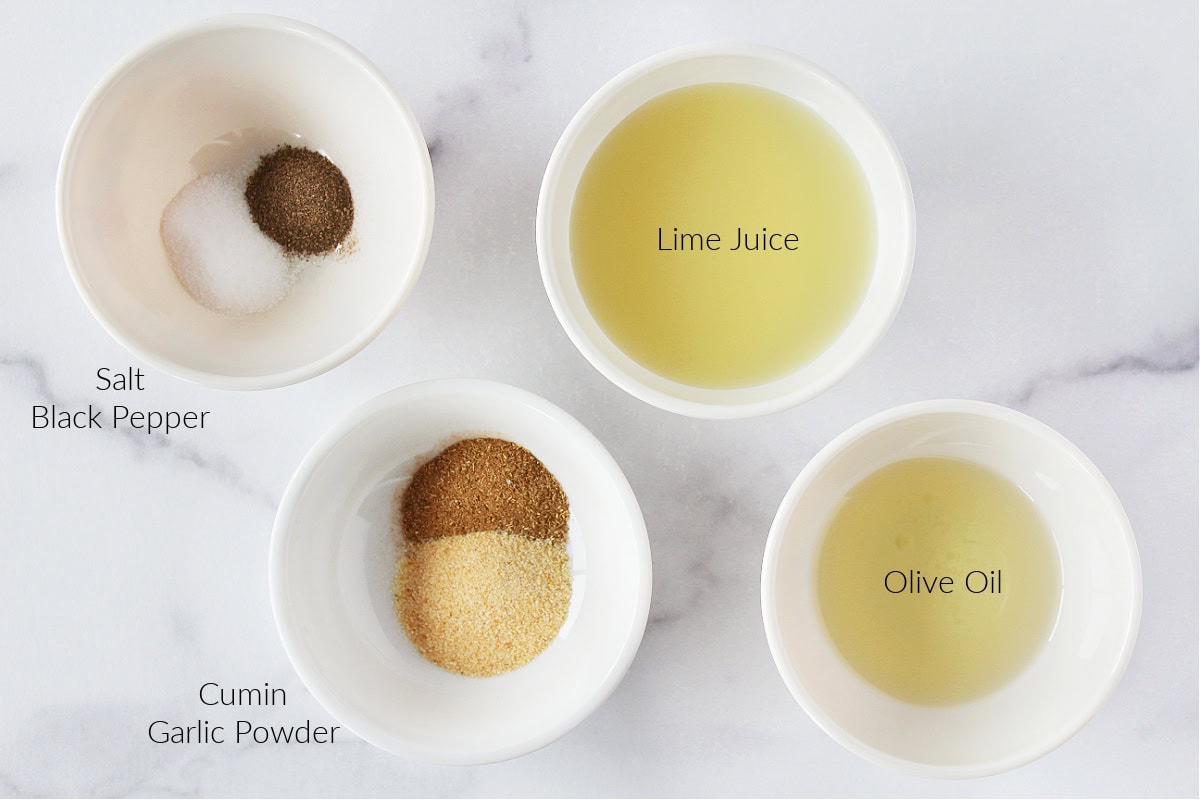 Lime juice, olive oil, cumin, garlic, salt and black pepper in bowls.