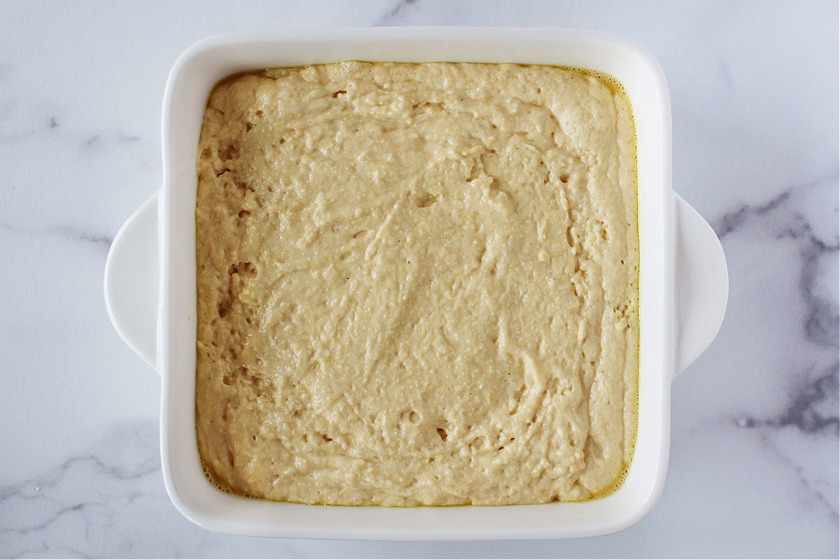 Cornbread batter in a square white baking dish.