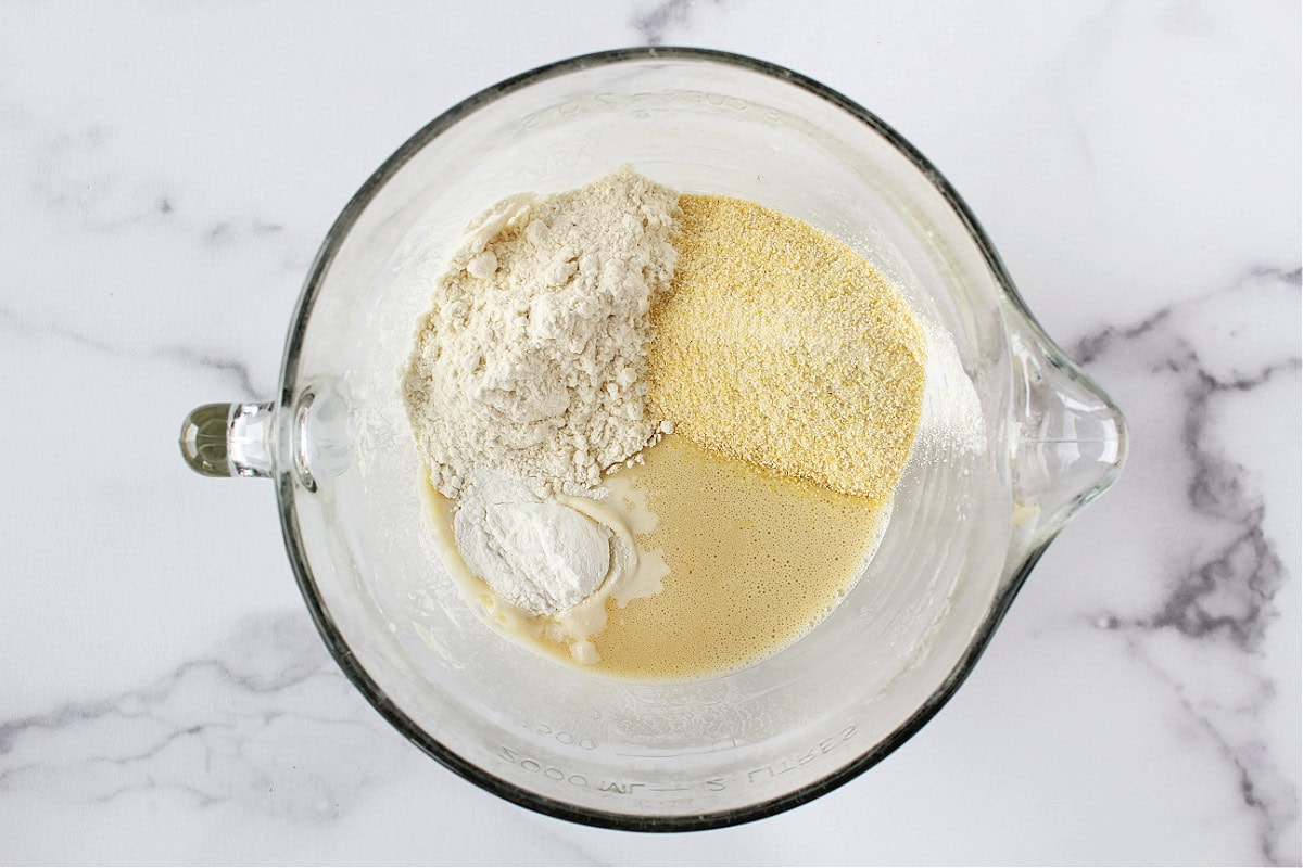 Cornmeal, flour and leaveners on top of wet ingredients in a mixing bowl.