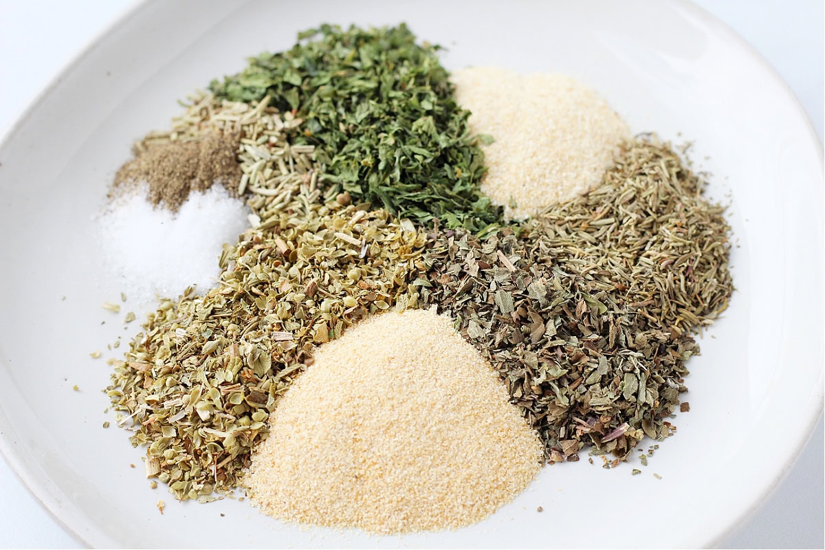 Dried seasonings and spices for Italian seasoning poured onto a white plate.