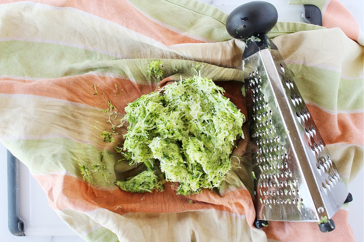 Finely shredded zucchini and a grater on a kitchen towel.