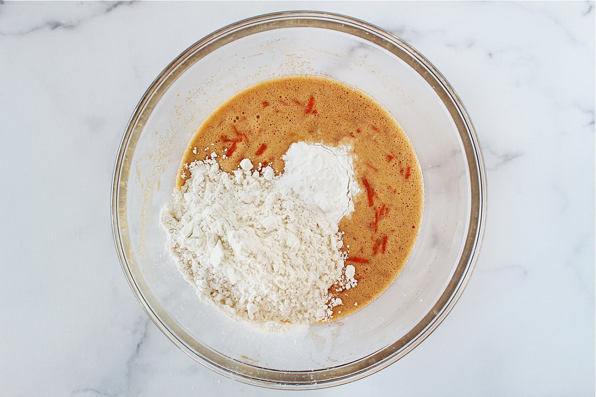 Gluten free flour and baking powder on wet ingredients in mixing bowl.