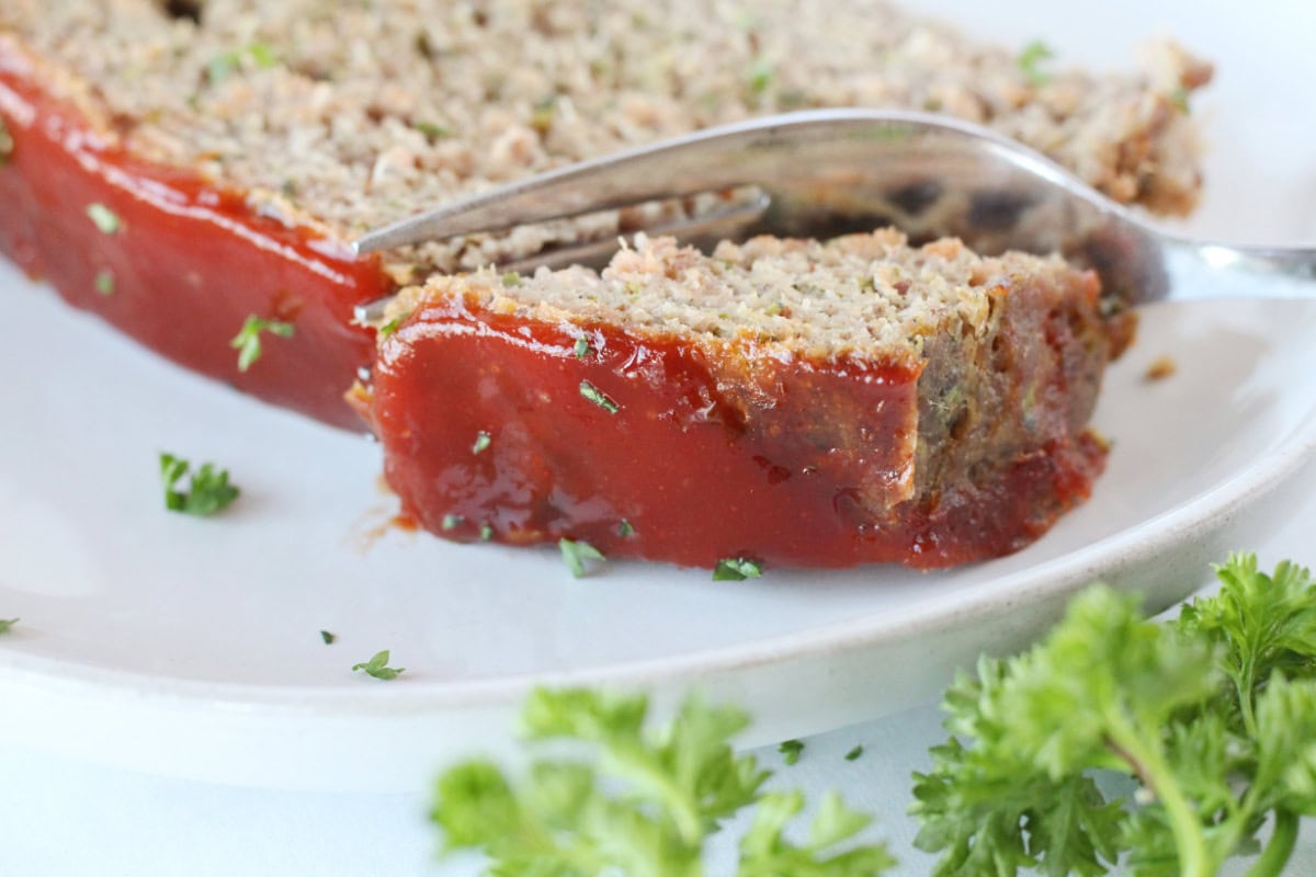 A fork slicing through a piece of whole foods meatloaf on a white plate.