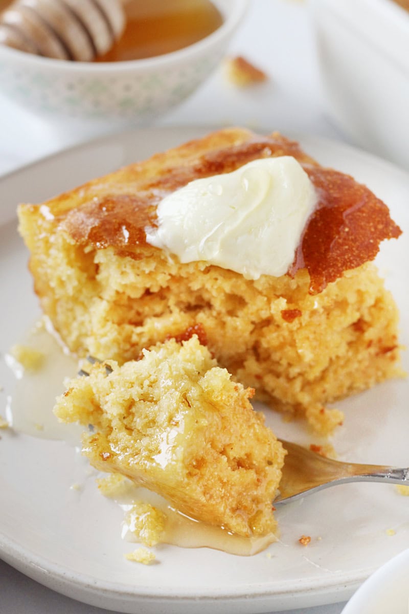 A fork slicing through a piece of cornbread topped with butter and honey.
