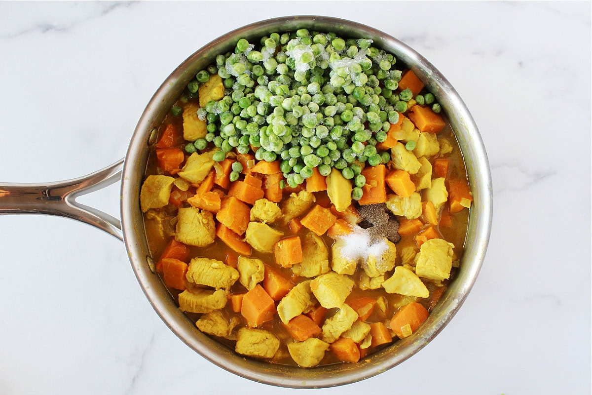 Frozen peas, salt and black pepper on top of chicken curry in a saute pan.