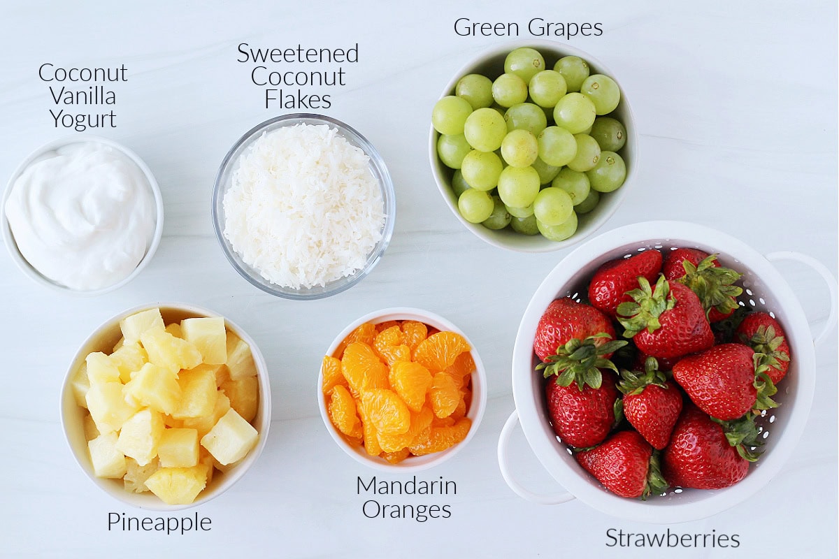 Bowls of labeled ingredients for a coconut Hawaiian fruit salad on a white countertop.