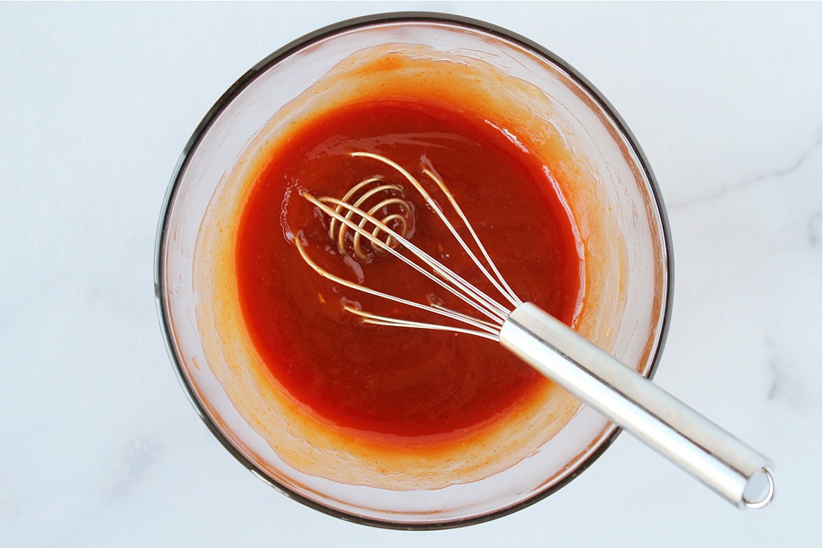 A whisk in a glass bowl holding ketchup meatloaf glaze.