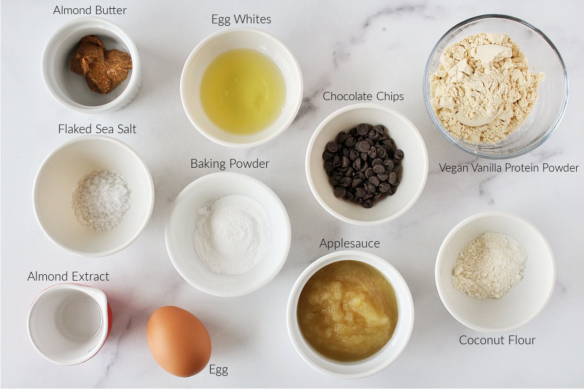 Labeled ingredients for chocolate chip cookie protein cake on a white marble countertop.