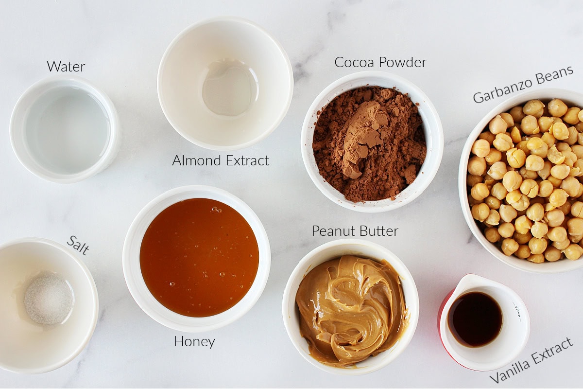 Labeled ingredients for brownie batter hummus on a white marble countertop.