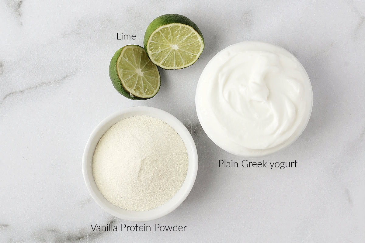 A lime sliced in half, vanilla protein powder and plain Greek yogurt on a countertop.