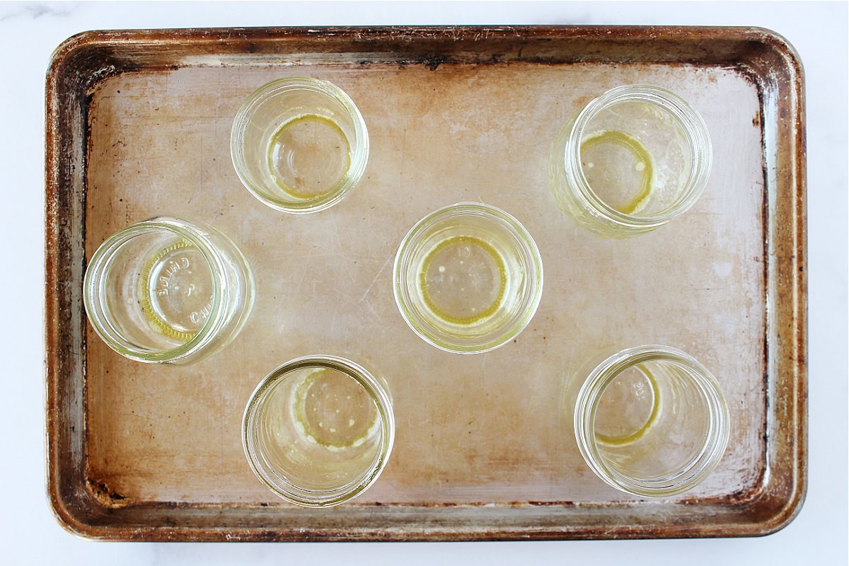 Six mason jars sprayed with nonstick cooking spray on a baking sheet.