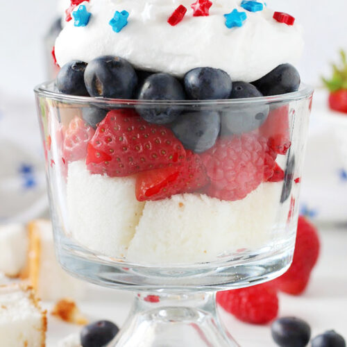 Angel food cake, raspberries and strawberries, blueberries and whipped topping and sprinkles in a cup.