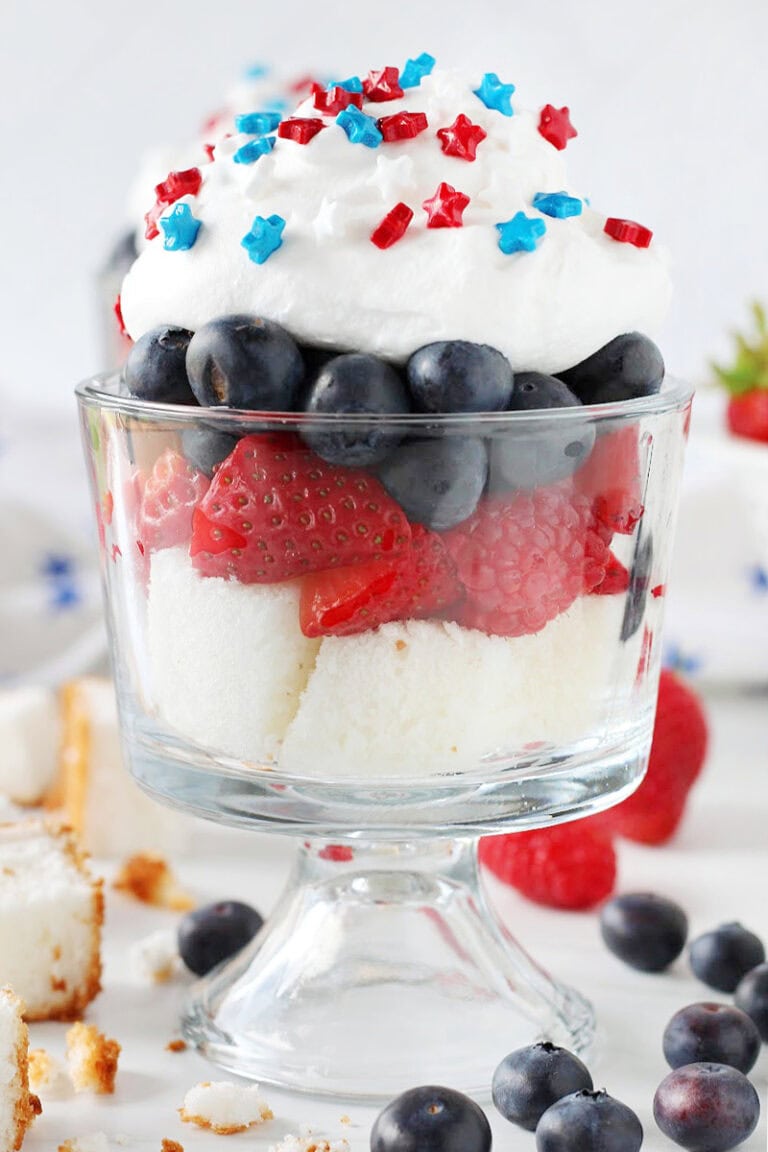 Angel food cake, raspberries and strawberries, blueberries and whipped topping and sprinkles in a cup.