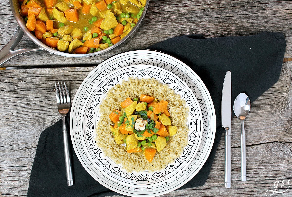 Chicken sweet potato curry with green peas on top of quinoa on a decorative plate.