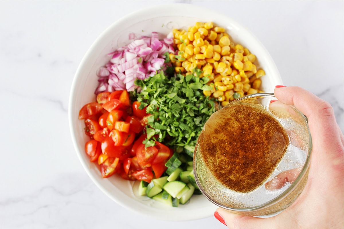 Pouring a lime dressing over a corn, tomato and cucumber salad.
