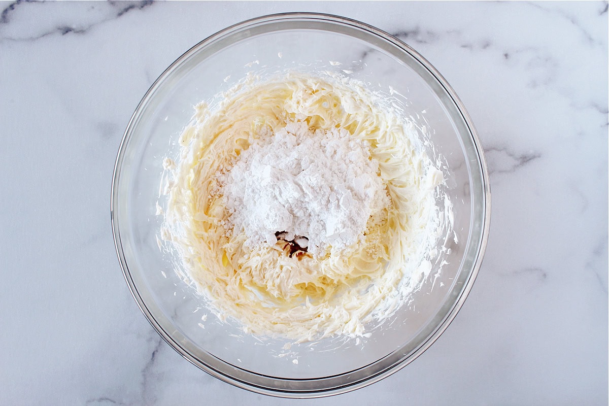 Powdered sugar and vanilla on creamed butter and cream cheese in a bowl.