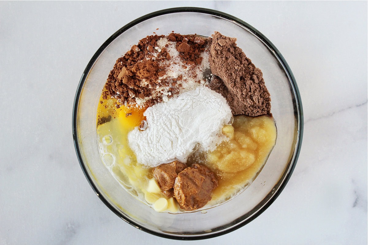 Chocolate protein powder, almond butter, coconut powder, egg, and applesauce in a bowl.
