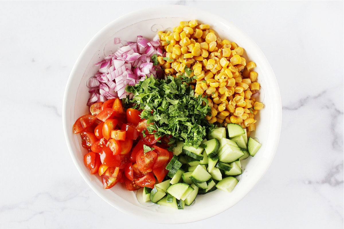 Roasted corn, red onion, tomato, cilantro and cucumbers in a bowl.