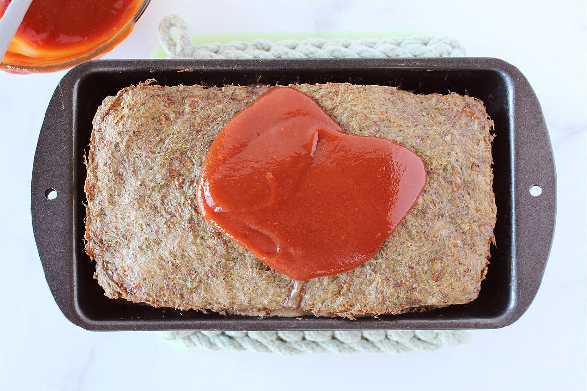 Ketchup glaze on top of baked meatloaf in a 9x5 metal pan.