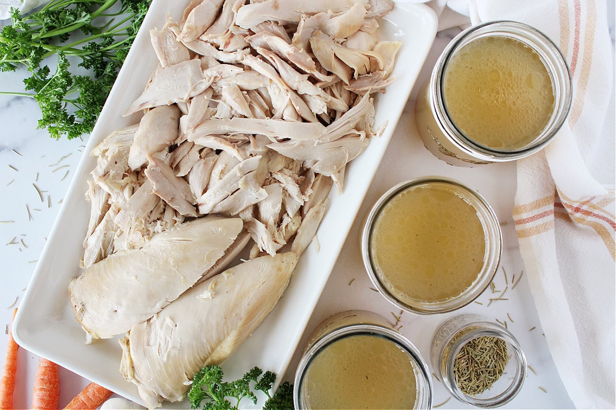 Shredded chicken on a white platter and three jars or homemade chicken broth.