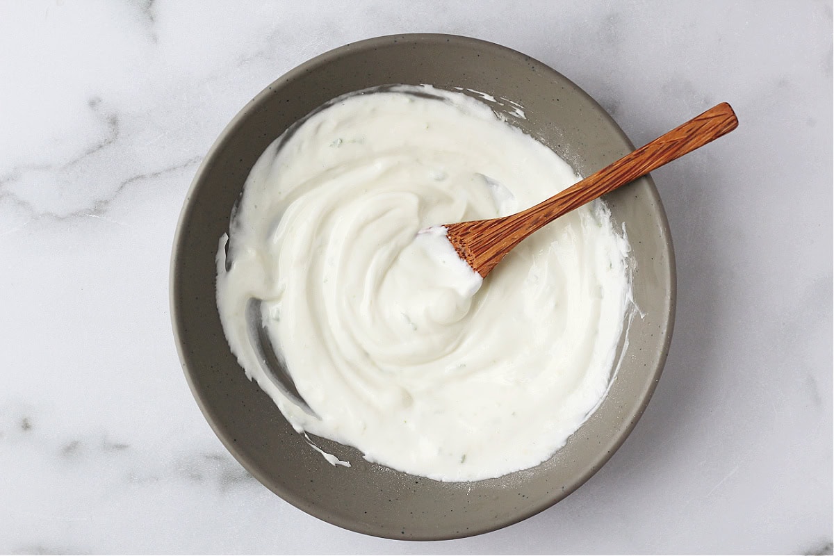 A bamboo spoon stirring yogurt in a grey bowl.