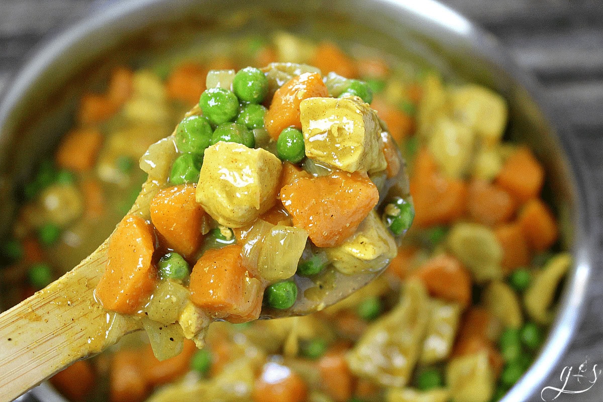 Chicken breast, green peas, and sweet potato in a curry sauce on a wooden spoon.