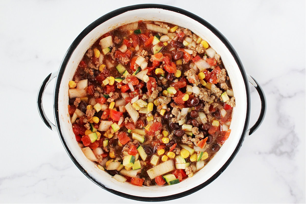 Black beans, diced veggies, ground beef and diced tomatoes in a soup pot.