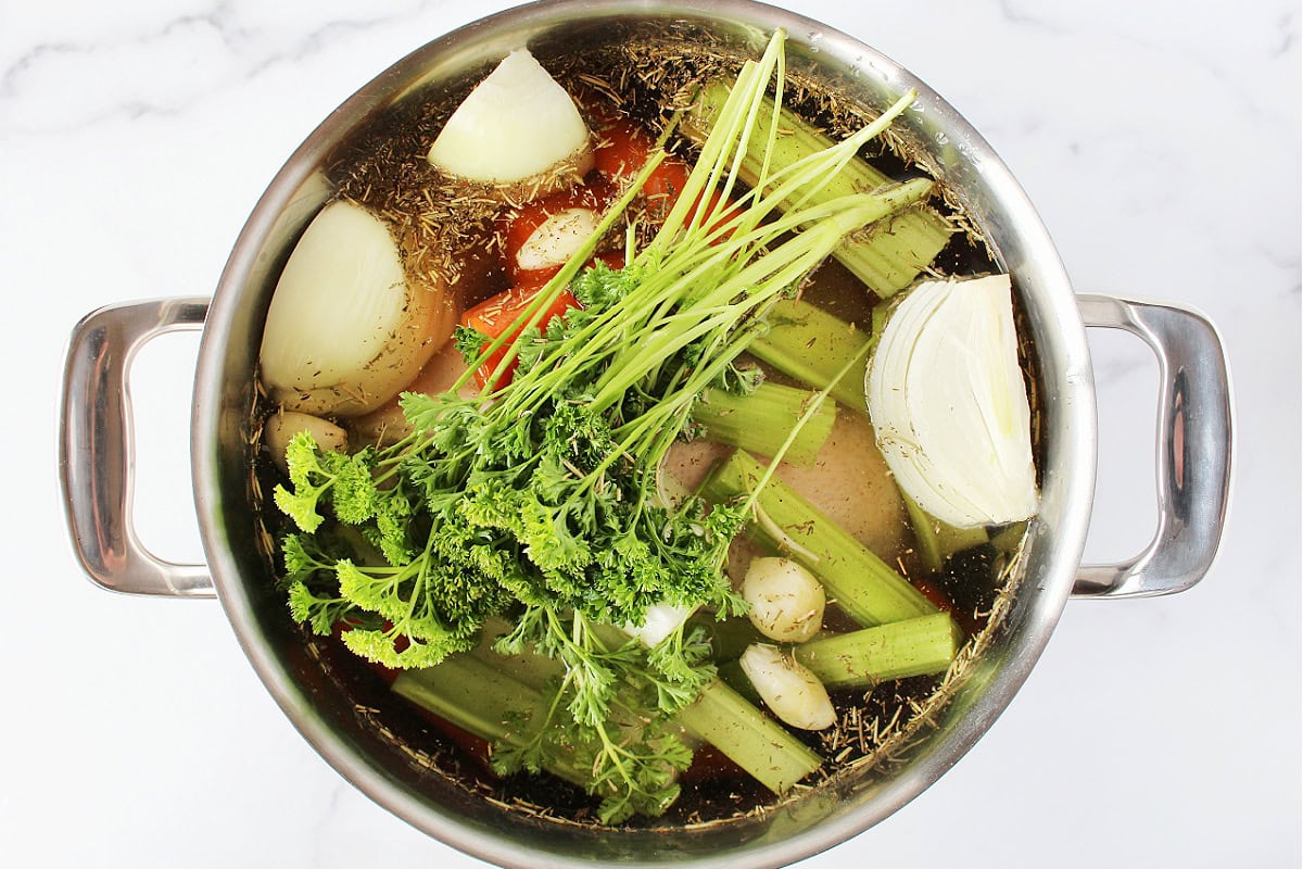 Water, herbs, sliced veggies and a whole chicken in a large soup pot.