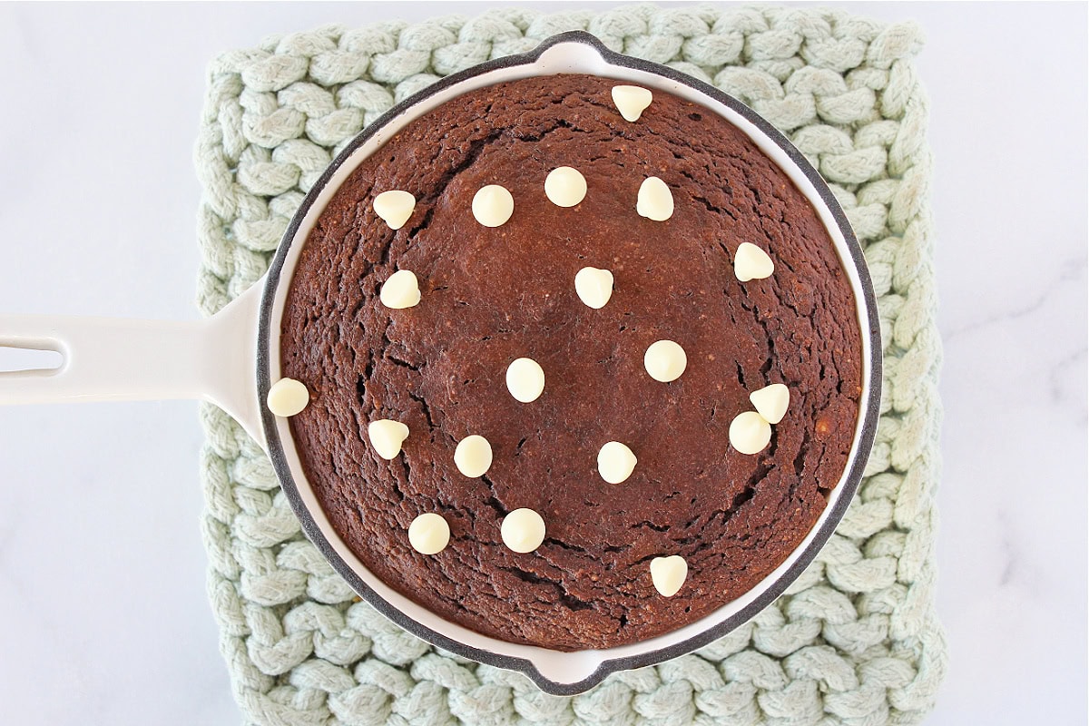White chocolate chips on top of a chocolate protein cake in a cast iron skillet.