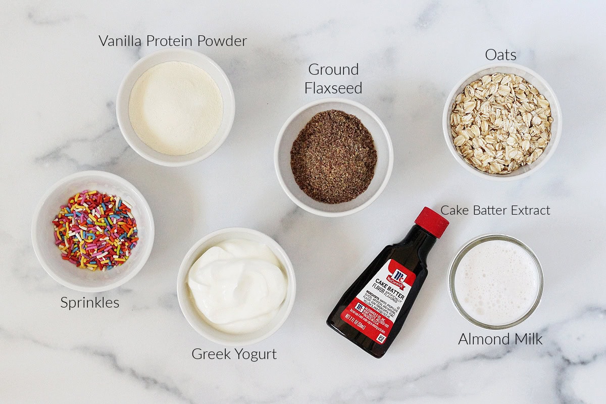 Labeled ingredients for funfetti blended overnight oats on a white marble countertop.